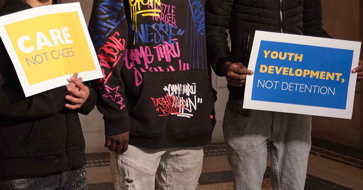 Nebraska youth hold signs at the Nebraska State Capitol with messages that include Care not cages and Youth development not detention.