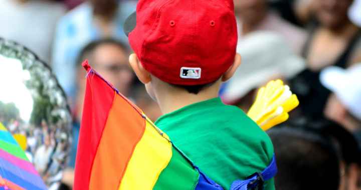 A child stands near a Pride flag.