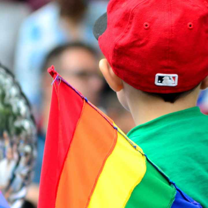 A child stands near a Pride flag.